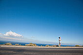 Woman Running along Asphalt Road by Ocean