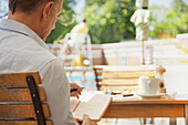 Rückenansicht eines Mannes, der in einem Café im Freien auf einem Notizblock schreibt