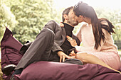 Paar auf großem Kissen im Park sitzend, küssend