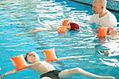 Kinder im Hallenbad, die mit einem Schwimmlehrer schwimmen lernen