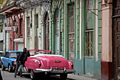 Kuba,Havanna,ein Mann in Schwarz lehnt an einem alten amerikanischen Cabrio aus den 1950er Jahren in rosa