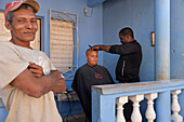 Kuba, Trinidad, ein Mann schneidet einem jungen Mann vor einem Haus die Haare.