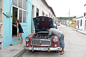 Kuba,Gibara,eine Frau betritt ihr Haus, während ein Mann den Motor seines alten amerikanischen Autos aus den 50er Jahren repariert