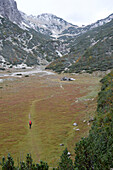 Österreich,Steiermark,ENNSTAL Alpen, ein Mann allein mit einem roten Rucksack wandert auf einem Hochplateau in Richtung Admonter Hütte