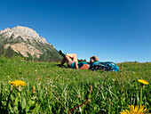 France,isÃ¨re,a woman dressed in shorts is lying in the grass at alpine pasture of Emeindras dessus 1420m at the bottom of the highest summit of the Chartreuse range Chamechaude 2082m