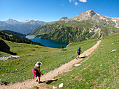 France,Alps,savoie,a woman  and a man are hikking on a moutain trail overlooking the lake of the Plan d