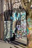 France,Paris,75,10th ARRT,Rue Jean Poulmarch; leading to the Canal Saint Martin,teenager sitting on the stairs in front of a wall covered with graffitis and paintings.