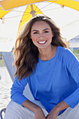 Woman in blue jumper and white trousers sitting on the beach