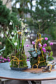 Schneeglöckchen (Galanthus) und Alpenveilchen (Cyclamen) dekoriert mit Zweigen und Moos als Gesteck