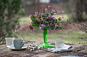 Flower bowl of cyclamen and willow catkins (Salix caprea) as decoration with glasses and coffee cup on garden table