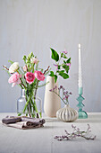 Wooden table with flower arrangement in glass and porcelain vases with twisted candle and linen napkins