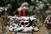 Snow-covered Advent arrangement in a metal basket with red candles and pine cones