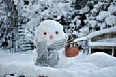 Schneemann mit grauem Schal und Korb im verschneiten Garten