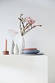 Magnolia in a vase with pastel-coloured crockery on a white pedestal