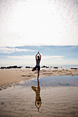 Rückenansicht einer Frau, die am Strand Yoga übt