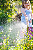 Junges Mädchen bewässert Blumen mit Gartenschlauch