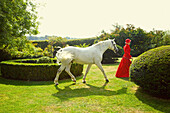 Woman in Red Equestrian Outfit Walking in Garden with Horse