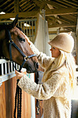 Young Woman Stroking Horse in Stable