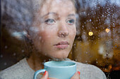 Woman Holding Drinking Cup behind Rainy Window