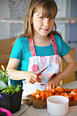 Lächelndes junges Mädchen schneidet Tomaten