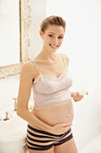 Smiling Pregnant Woman Applying Beauty Cream on her Stomach