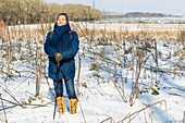 Frau steht auf einem verschneiten Feld und hält einen Wanderstock