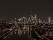 Luftaufnahme von beleuchteten Wolkenkratzern im Stadtbild entlang des Mains bei Nacht, Frankfurt, Deutschland