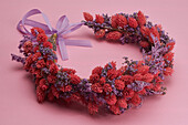 Still life beautiful red and purple dried flower crown on pink background