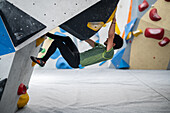 Young man in his twenties climbing on a climbing wall indoors