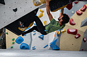 Junger Mann in den Zwanzigern beim Klettern an einer Kletterwand in einer Halle