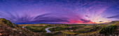 A panorama of the landscape and sky at sunset at Writing-on-Stone Provincial Park (Áísínai'pi) in Alberta, with the Milk River below winding amid the sandstone rock formations, and the Sweetgrass Hills in the distance in Montana. Note the people at far right for scale.