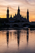 Die Kathedrale-Basilika Unserer Lieben Frau von der Säule spiegelt sich bei Sonnenuntergang im Fluss Ebro, Zaragoza, Spanien