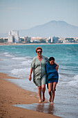 Grandmother walks with her granddaughter and hugs her on Peñiscola Beach, Castellon, Valencian Community, Spain