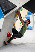 Young man in his twenties climbing on a climbing wall indoors