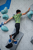 Young man in his twenties climbing on a climbing wall indoors