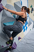 Young man in her twenties climbing on a climbing wall indoors