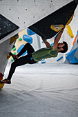 Young man in his twenties climbing on a climbing wall indoors