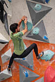 Young man in his twenties climbing on a climbing wall indoors