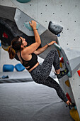 Young man in her twenties climbing on a climbing wall indoors