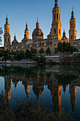 Die Kathedrale-Basilika Unserer Lieben Frau von der Säule spiegelt sich bei Sonnenuntergang im Fluss Ebro, Zaragoza, Spanien