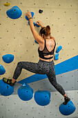 Young man in her twenties climbing on a climbing wall indoors