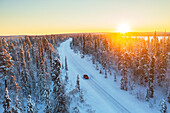 Car travels the icy and empty road crossing the boreal snowy forest at sunrise, Swedish Lapland, Sweden, Scandinavia, Europe