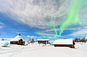 Typical wooden buildings covered with snow under the Northern Lights (Aurora Borealis), full moon night, Kilpisjarvi, Enontekio municipality, Finnish Lapland, Finland, Scandinavia, Europe