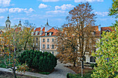 View of traditional low-rise roof-tiled houses behind a park area under blue sky with clouds, Warsaw, Poland, Europe