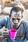 Staubbedeckter Mann trinkt lokalen Kaffee, Mundari-Stamm, Südsudan, Afrika