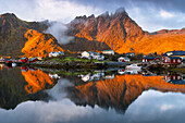 Reflections of houses and mountains in the water at Ballstad village during sunrise, Vestvagoy, Nordland, Lofoten Islands, Norway, Europe