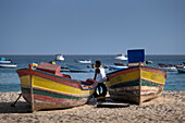 Einheimischer ruht sich zwischen bunten Fischerbooten am Strand Praia de Santa Maria aus, Santa Maria, Sal, Kapverdische Inseln, Atlantik, Afrika