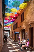 France, Var, Saint-Raphaël, Arts district, papier-mâché sculpture by artist Liliana Anic and multicolored umbrellas hanging over rue du Safranier