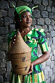 Rwanda, Volcanoes National Park, young Rwandan woman in traditional dress, member of staff of Bisate Lodge, carrying a basketry