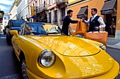 Italy, Lombardy, Milan, Fashion Quadrilateral (Quadrilatero della moda), Alfa Romeo Duetto Spider yellow cabriolet in front of the Four Seasons Hotel Milano, the doorman brings a Vuitton bag